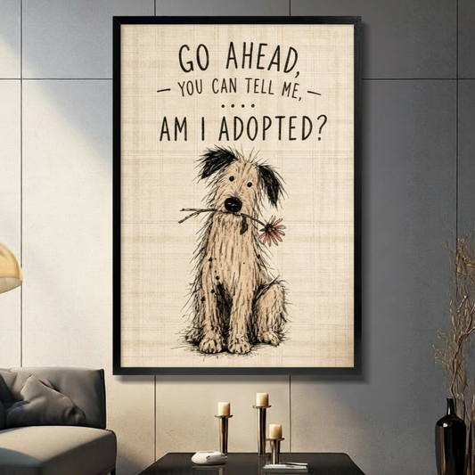Black framed funny am I adopted shaggy dog holding a daisy canvas art with hand-drawn sketch style and go ahead you can tell me am I adopted quote on a vintage linen-textured beige background, displayed on a dark gray tile wall above a console table with pillar candlesticks beside a charcoal sofa