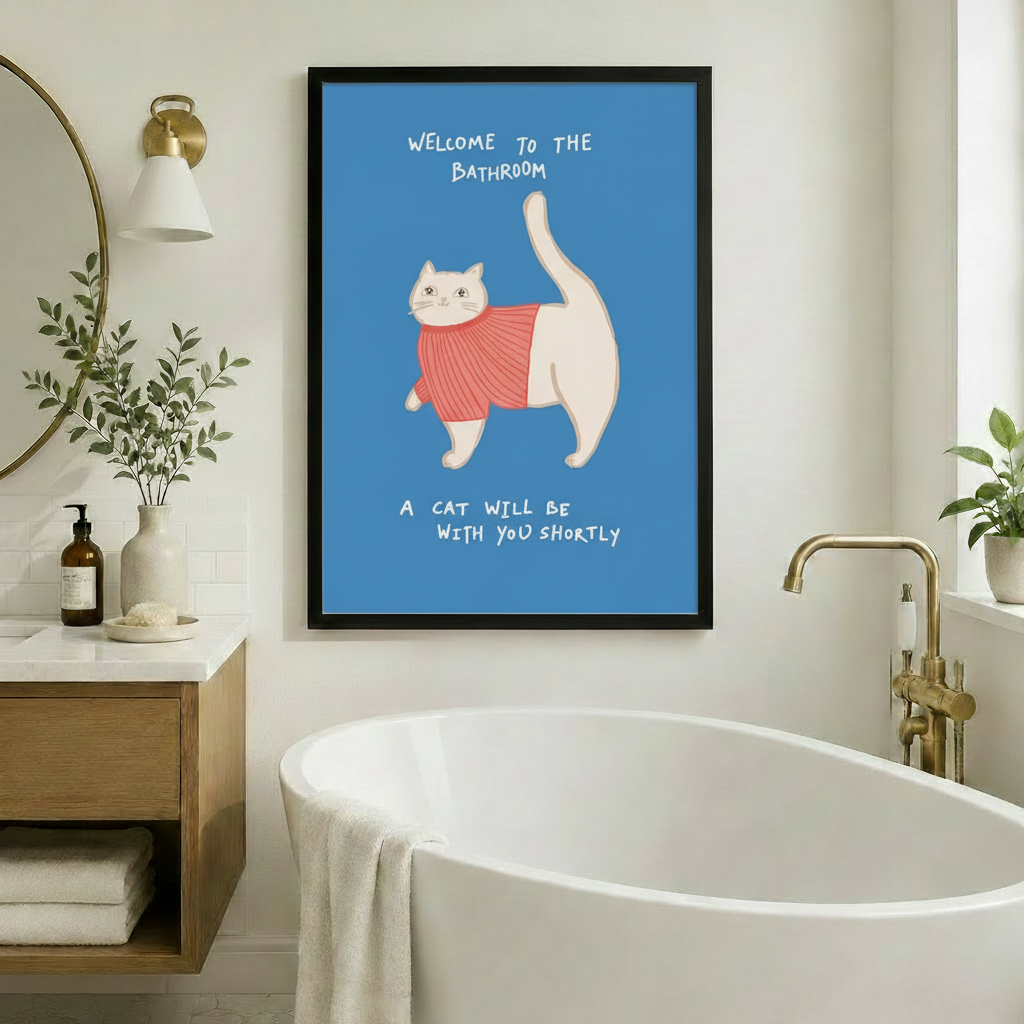 Framed funny whimsical illustration chubby white cat wearing pink ribbed turtleneck sweater with tail raised high and bold handwritten text Welcome To The Bathroom A Cat Will Be With You Shortly on steel blue background canvas print on warm beige wall beside white freestanding soaking bathtub with brass floor faucet round mirror and eucalyptus branches - humorous bathroom cat sweater welcome wall art for spa-style bathroom decor