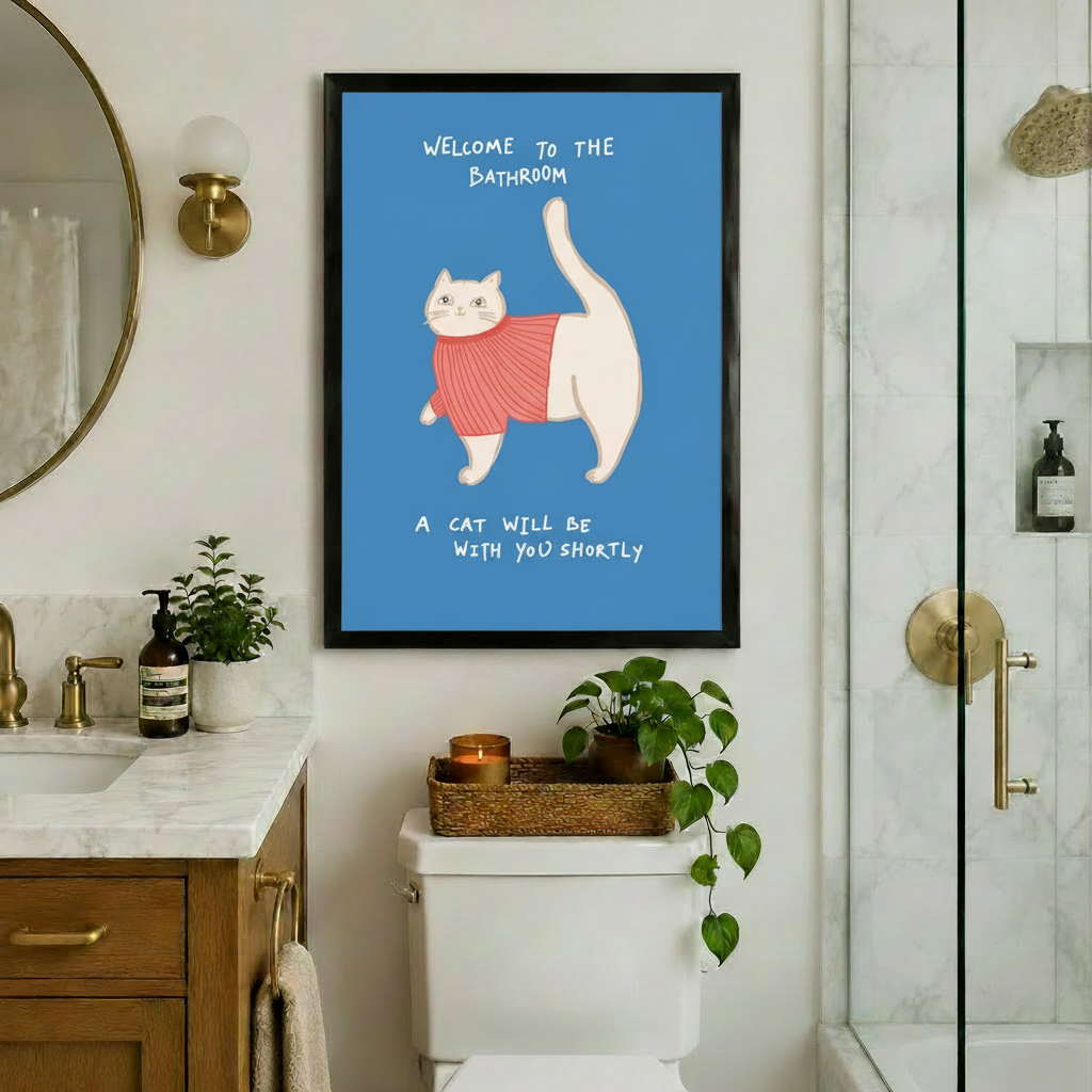 Framed funny whimsical illustration chubby white cat wearing pink ribbed turtleneck sweater with tail raised high and bold handwritten text Welcome To The Bathroom A Cat Will Be With You Shortly on steel blue background canvas print on white wall above white toilet with wicker tray amber candle and trailing potted plant beside marble vanity with brass fixtures and glass shower - humorous bathroom cat sweater welcome wall art for luxury bathroom decor