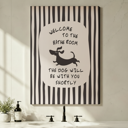 Stretched canvas wall art of a whimsical bathroom quote print with bold black and white vertical stripes framing a central oval with hand-lettered welcome to the bathroom text above a leaping cartoon dachshund silhouette and the humorous quote the dog will be with you shortly displayed above a minimalist black faucet sink with a soap dispenser and small potted plant