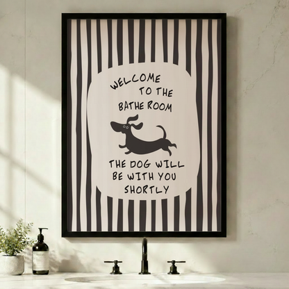 Black framed funny bathroom dachshund stripe canvas art with bold black and white vertical stripes and a central oval featuring hand-lettered welcome to the bathroom above a running cartoon dachshund silhouette and the quote the dog will be with you shortly in a minimalist black and white bathroom above a sink with a black faucet and soap dispenser