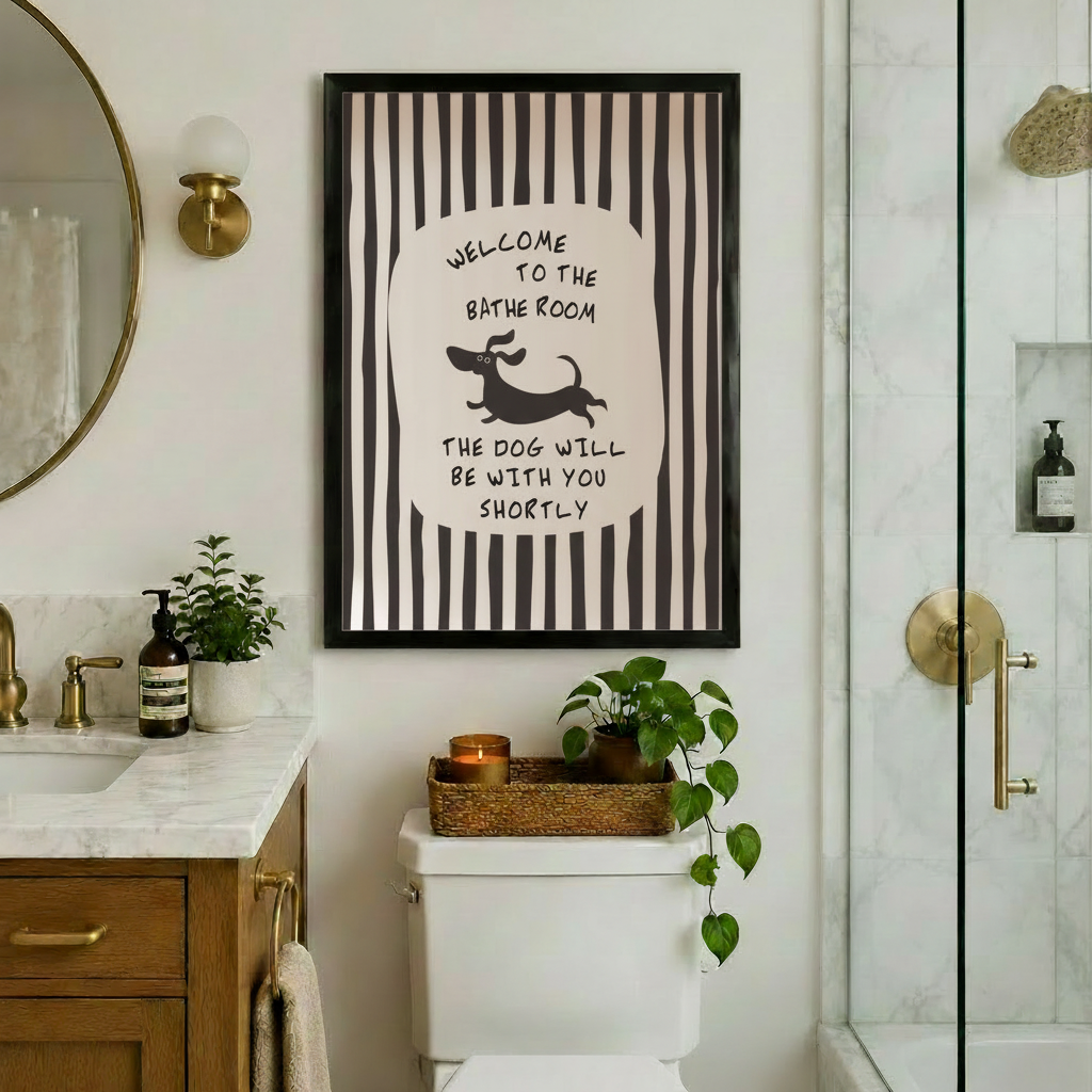 Black framed funny dachshund bathroom quote canvas art with bold black and white vertical stripes and a central oval with hand-lettered welcome to the bathroom above a running cartoon dachshund and the text the dog will be with you shortly hung above a toilet in an elegant bathroom with marble countertops, a wood vanity, gold hardware, a round mirror, and lush green plants