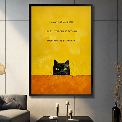 Black framed funny black cat peeking over a textured orange ledge canvas art with bold always be yourself unless you can be batman then always be batman quote on a vivid yellow background, displayed on a dark gray wall above a console table with tall candlesticks beside a charcoal sofa