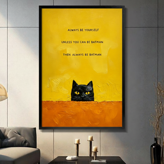 Black framed funny black cat peeking over a textured orange ledge canvas art with bold always be yourself unless you can be batman then always be batman quote on a vivid yellow background, displayed on a dark gray wall above a console table with tall candlesticks beside a charcoal sofa