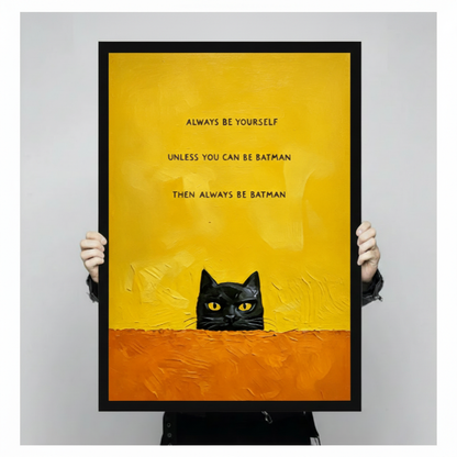 Person holding a large black framed funny black cat canvas art print with a curious cat peeking over an orange ledge and always be yourself unless you can be batman then always be batman text on a bold yellow background against a light gray studio backdrop