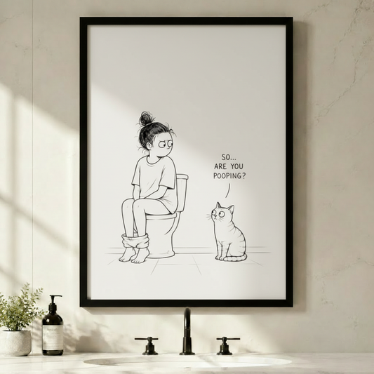 Framed black and white line art canvas of a girl sitting on a toilet with a curious cat asking "So... Are You Pooping?", hung above a minimalist bathroom sink
