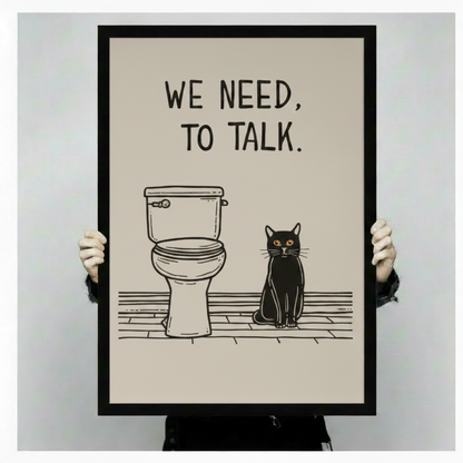 Person holding a large vertical black framed funny we need to talk black cat bathroom canvas art print showing bold blocky hand-lettered we need to talk text above a simple line art toilet and a stern black cat with amber eyes seated on a sketched wood floor in a minimalist black and warm cream palette against a light gray background