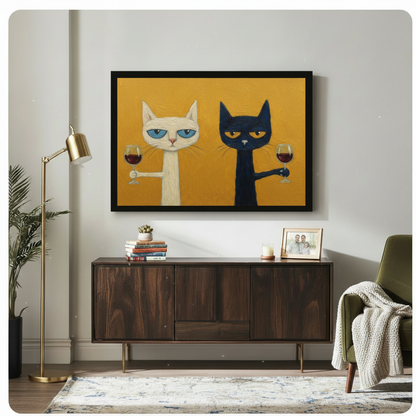 Black framed funny cats drinking wine canvas art showing a sulky white blue-eyed cat and a grumpy black amber-eyed cat each raising a red wine glass on a bold mustard yellow oil-painted background, displayed above a dark walnut sideboard with a gold floor lamp and olive green armchair