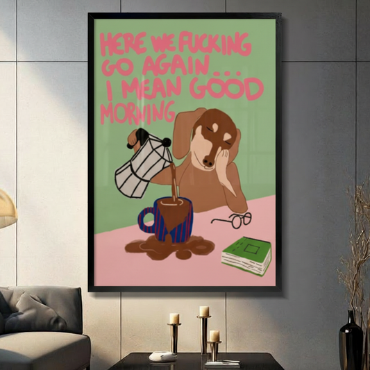 Black framed funny sleepy dachshund pouring coffee canvas art with a drowsy brown wiener dog resting its cheek while spilling coffee from a moka pot, glasses and a green book nearby, and a bold pink here we go again I mean good morning quote on a green and pink background, displayed on a dark gray tile wall above a black table with candlesticks beside a gray sofa