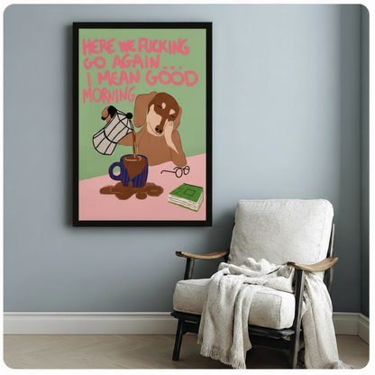Black framed whimsical sleepy dachshund coffee canvas art featuring a tired brown wiener dog leaning on its paw while coffee spills over the mug, with reading glasses, a green book, and a cheeky good morning quote in pink lettering on a green and pink background, displayed on a soft blue-gray wall beside a white upholstered folding armchair draped with a cream throw blanket