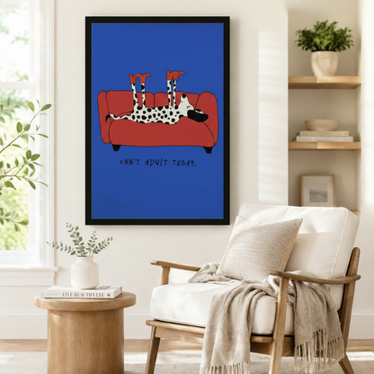 Framed "Can't Adult Today" Dalmatian wall art in cobalt blue beside a white linen armchair with a throw blanket in a Scandinavian-style living room