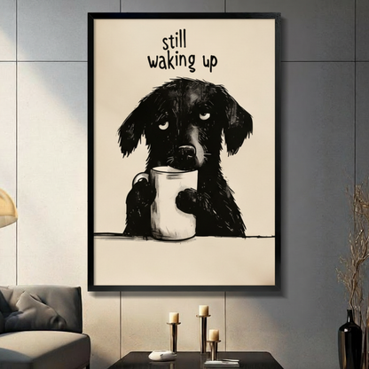 Funny illustration sleepy black dog holding white coffee mug with drowsy eyes "Still Waking Up" quote black framed canvas art on warm beige background on a dark gray paneled wall above a charcoal sofa with brass candle holders and a black decorative vase