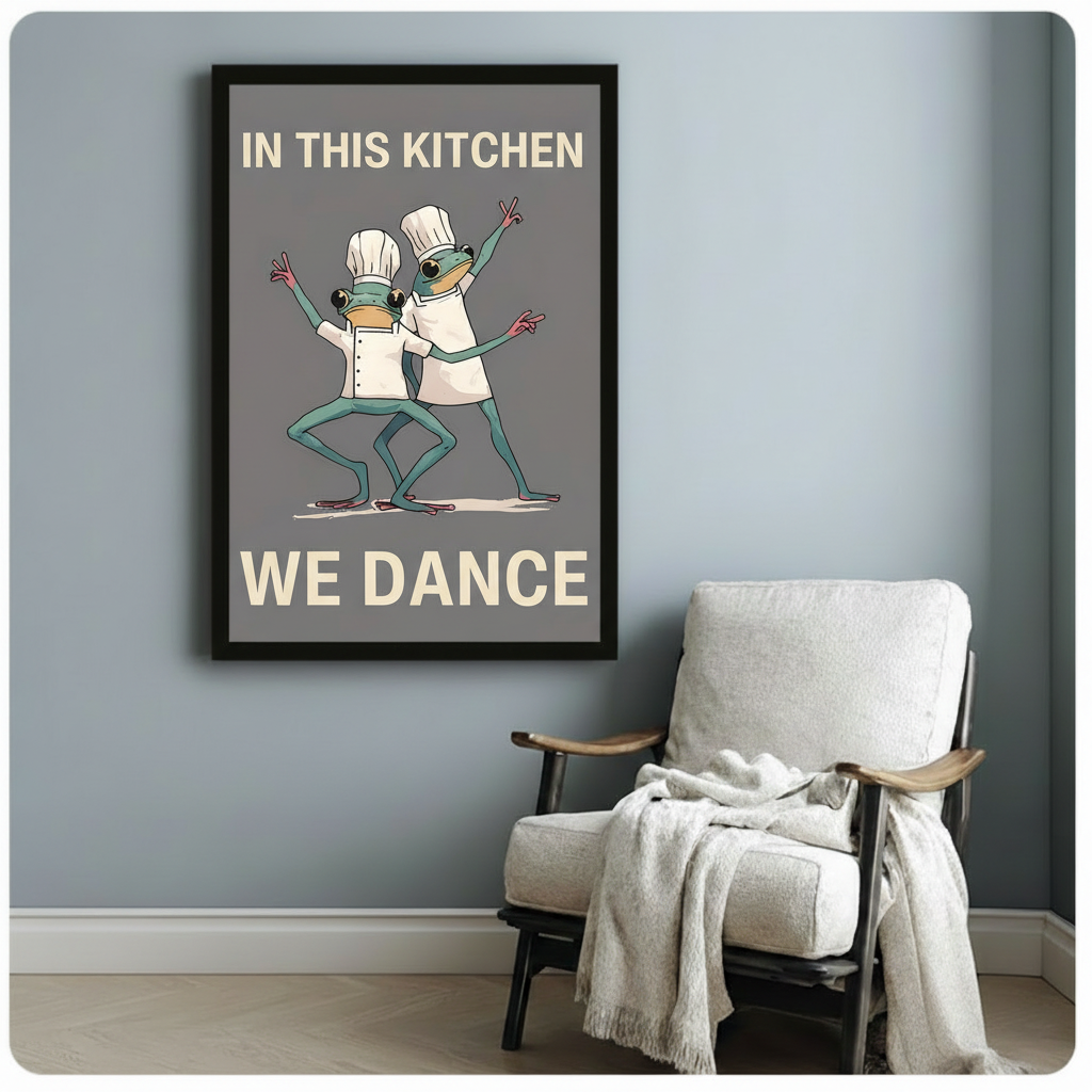 Black framed funny frog chef kitchen dance canvas art print with two dancing green frogs in white chef hats and the quote In This Kitchen We Dance in bold cream text on grey background on a blue-grey wall beside a white linen armchair with draped throw
