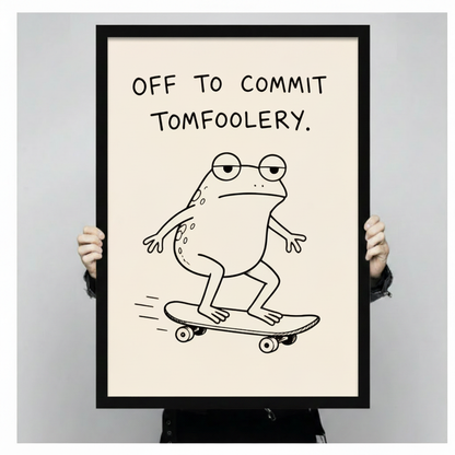 Person holding a large black framed minimalist funny frog skateboard canvas art print showing print size scale with a deadpan round frog in glasses on a skateboard and the quote Off To Commit Tomfoolery in black handwritten font on cream background