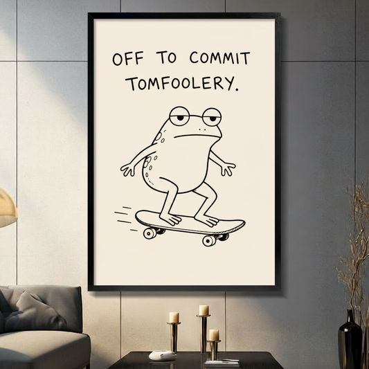Framed minimalist line drawing canvas wall art of a chubby frog wearing round glasses riding a skateboard with the humorous quote Off To Commit Tomfoolery in bold black handwritten text on a cream background on a dark grey wall in a modern living room