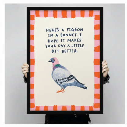 Cute pigeon in pink bonnet with "I hope it makes your day a little bit better" funny quote framed wall art print held up for size reference against a light gray neutral background with vibrant orange pink striped frame border