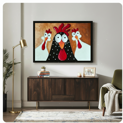 Black framed funny rooster and two chickens canvas art showing three wide-eyed cartoon birds — a bold black polka-dot rooster with a red comb between two white hens on a warm golden brown textured background, displayed above a dark walnut sideboard with a gold floor lamp and olive green armchair