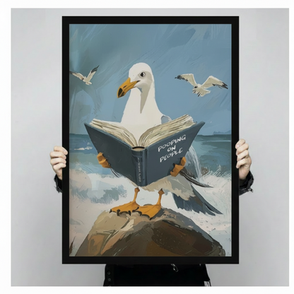 Person in black clothing holding large black framed canvas print of seagull reading Pooping on People book on seaside rock