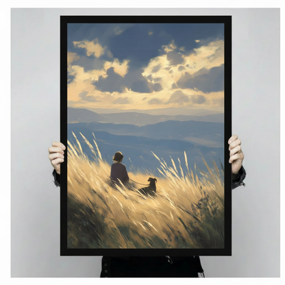 Hand-held display of a black-framed canvas art print featuring an oil painting of a girl and her dog sitting side by side in glowing golden tall grass with dramatic clouds and blue mountain panorama — serene nature wall art