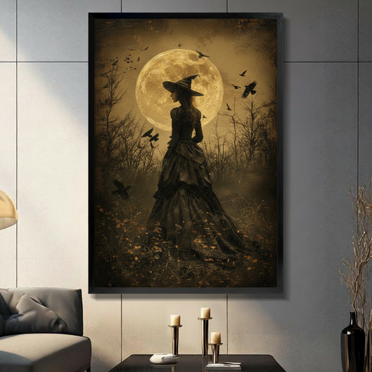 Dark gothic oil painting of a mysterious witch in a dramatic layered black Victorian gown and wide-brim pointed hat standing with her back to the viewer in a barren winter landscape with gnarled bare trees surrounding her a massive glowing golden full moon forming a luminous halo behind her silhouette and multiple black ravens in flight scattered across the amber-toned sky aged textured dark academia wall art framed print displayed in a living room with dark gray sofa, pillar candle holders, and black decor