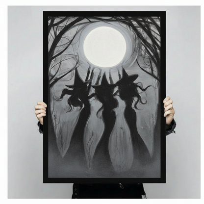 Hands in black sleeves holding a large black framed three witches full moon canvas art print against a neutral gray background, front-facing product size display