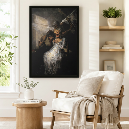 Framed dark romantic oil painting inspired by Goya featuring skeletal masked figures in white gown displayed beside a white armchair in a Scandinavian reading nook