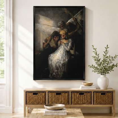 Framed Goya-style dark baroque oil painting of skeletal figures in white gown displayed above a wicker console table in a bright modern entryway