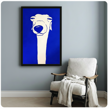 Black framed bold cobalt blue greyhound dog pop art canvas print with white minimalist line art dog illustration hung on a soft blue-gray wall beside a white linen wood armchair with a cream knit throw blanket