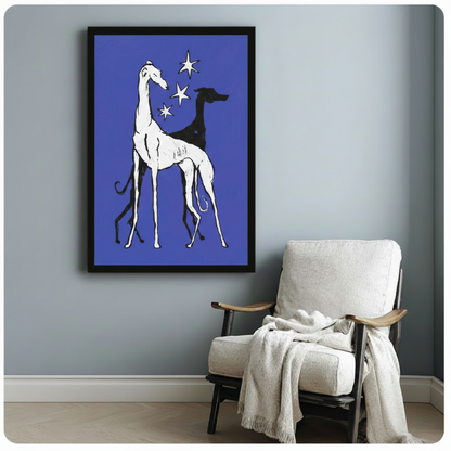 Black framed wall art print of two greyhounds and stars on blue background, styled beside white linen armchair

