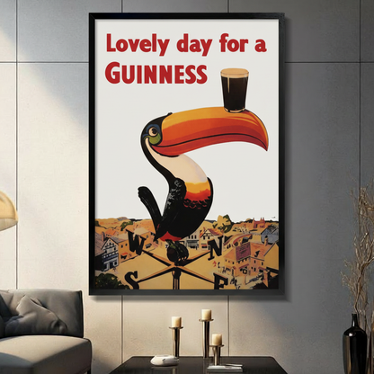 Black framed vintage Guinness toucan advertisement print displayed on a grey panelled wall in a modern living room with candle decor