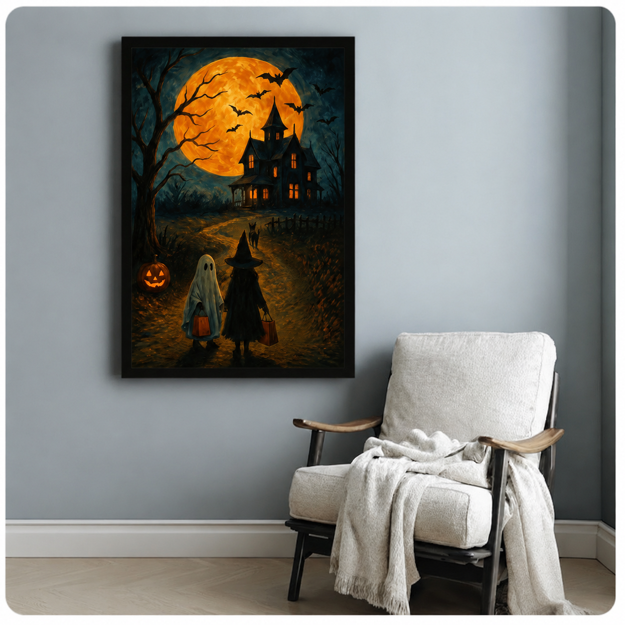 Spooky Halloween poster print with ghost, witch, and black dog walking toward a haunted house under a glowing orange full moon, black frame on grey wall beside armchair