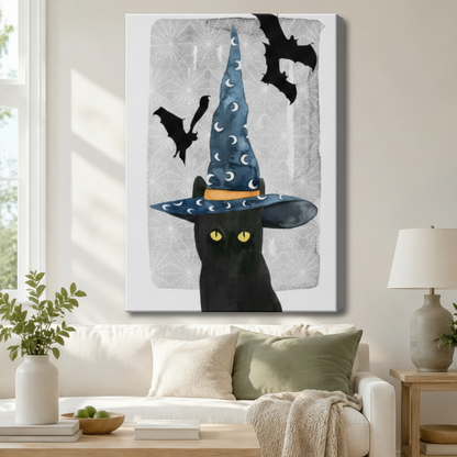 Stretched canvas Halloween witch black cat with bat wall art featuring a brooding black cat with piercing yellow eyes beneath a tall blue crescent moon witch hat with two black bats swooping overhead on a textured silver-gray watercolor background, hung above a white sofa with sage green pillows in a bright living room