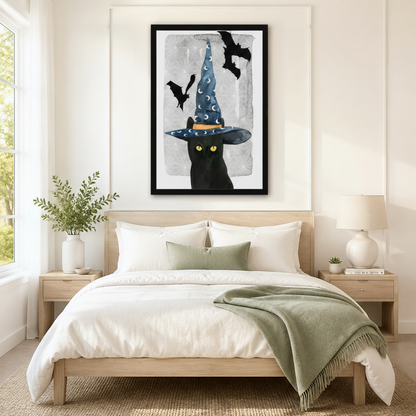 Black framed Halloween witch black cat with bat canvas art with a mysterious black cat with bright yellow eyes beneath a tall blue moon-print witch hat and two black bats soaring above on a textured crackled silver-gray watercolor background, hung above a light wood bed with white linen bedding and a sage green throw in a serene Scandinavian bedroom