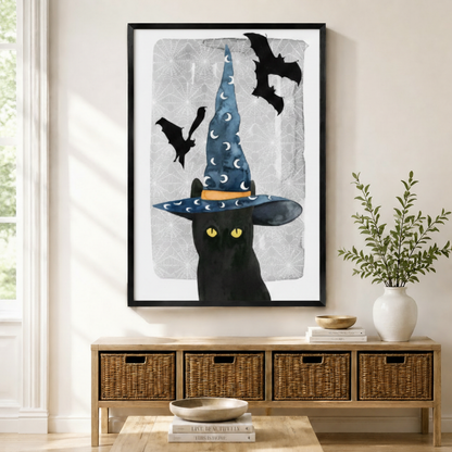 Black framed Halloween witch black cat with bat canvas art with a mysterious black cat with glowing yellow eyes wearing a tall blue moon-print witch hat surrounded by flying black bats on a crackled silver-gray watercolor background, displayed above a rattan storage console in a bright entryway