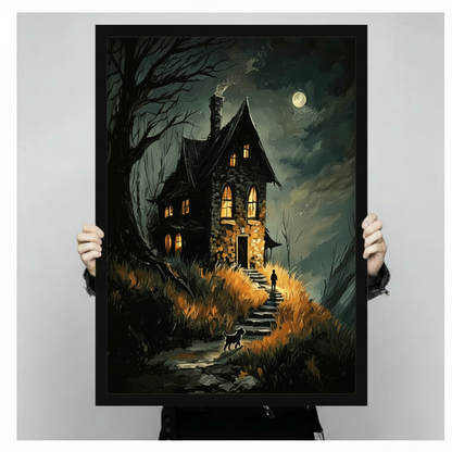 Close-up hand-held product shot of a framed dark gothic wall art print depicting a haunted stone house at night with amber-lit windows, a full moon, dead trees, and a black cat on a misty stone path