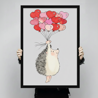 	Hand-held product shot of a black-framed art print showing a cute hedgehog with rosy cheeks clutching a bouquet of red and pink heart balloons