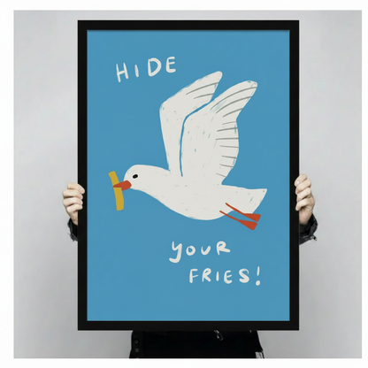"Hide Your Fries" seagull illustrated framed print held up to show full size, bold blue background with white bird and yellow chip detail
