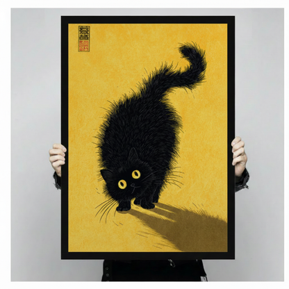 Person holding a large black framed Japandi style fluffy black cat canvas art print with a shaggy black cat with glowing yellow eyes in a low crouching pose casting a dramatic shadow on a warm golden amber textured background with a red Chinese seal stamp in the upper left corner