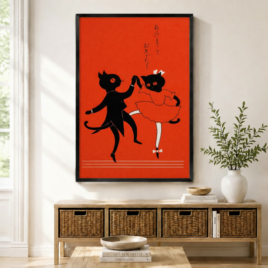 Black framed Japanese retro dancing cat couple wall art above a wicker storage console with white ceramic vases and green branches in a bright minimal entryway