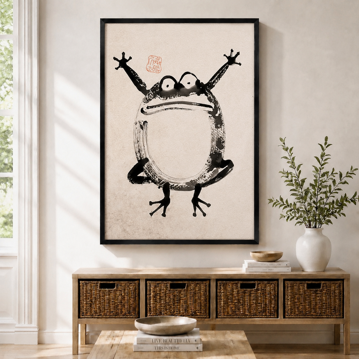 Framed Japanese ink wash frog wall art displayed above a wicker storage console in a bright Scandinavian-style entryway