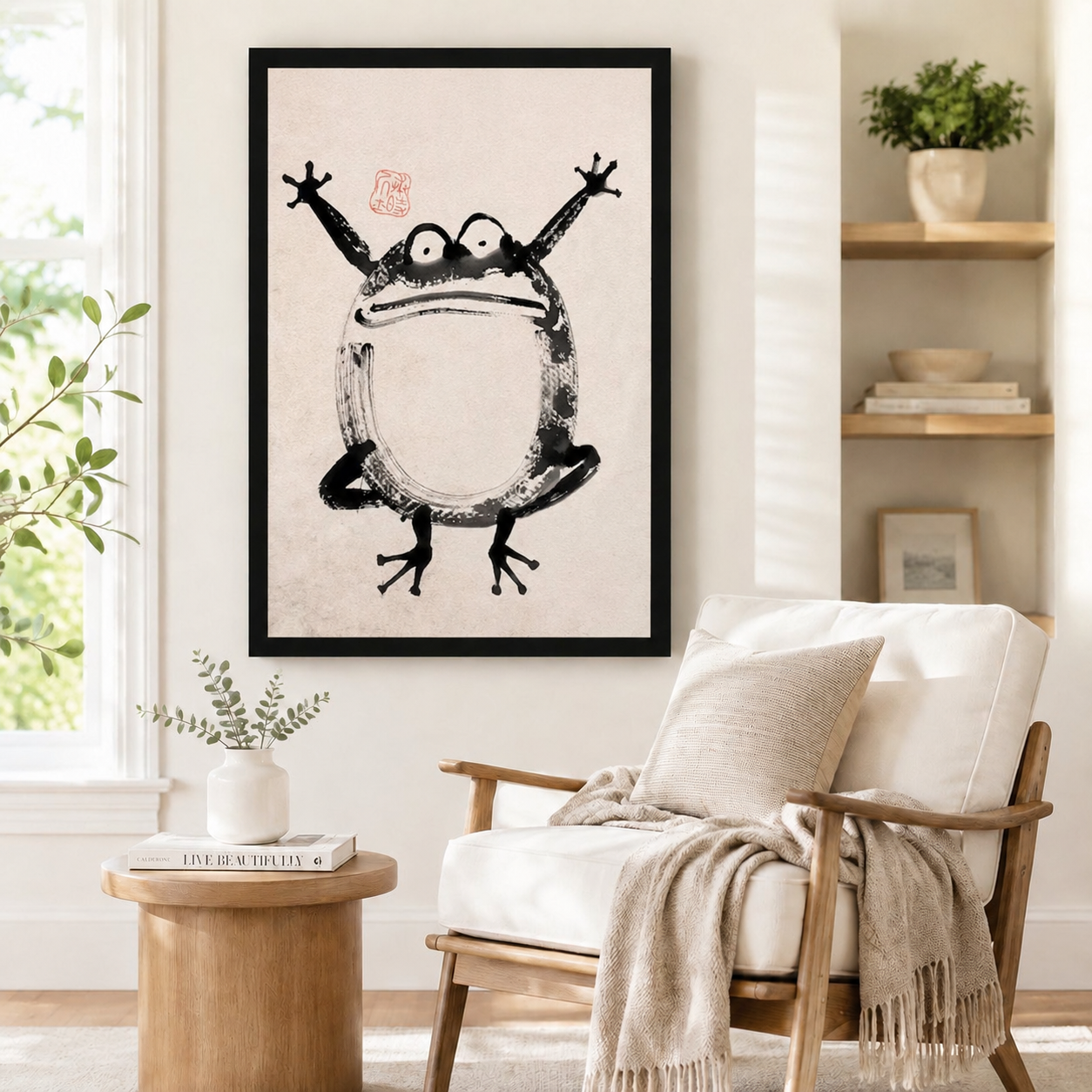 Black-framed Japanese ink frog poster art styled beside a wooden armchair and round side table in a minimalist reading nook

