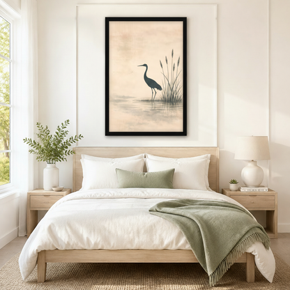 Black framed Japanese sumi-e ink wash heron and reed lake canvas art with a dark teal heron standing quietly in a still misty lake beside tall slender reeds and their soft water reflection on a warm peach aged parchment background, hung above a wooden bed frame in a sun-drenched Scandinavian bedroom with crisp white linen bedding, a sage green accent pillow, matching round nightstand lamps, and a white ceramic vase of greenery