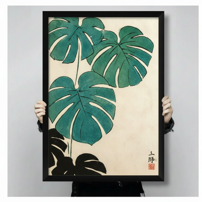 Japanese brush painting monstera canvas art in a black frame held up against a light gray background, showing teal leaves and ink seal detail