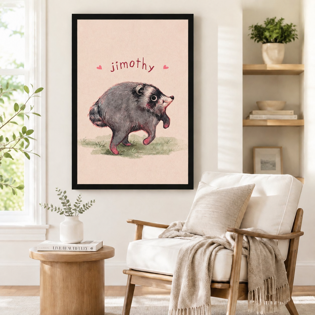 Black framed Jimothy opossum illustration print with pink heart accents mounted on a white wall above a linen armchair in a Scandinavian-style reading corner with natural wood side table
