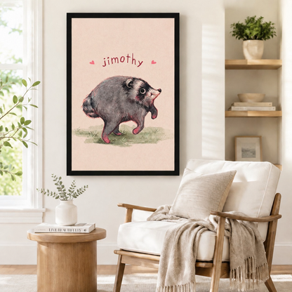 Black framed Jimothy opossum illustration print with pink heart accents mounted on a white wall above a linen armchair in a Scandinavian-style reading corner with natural wood side table