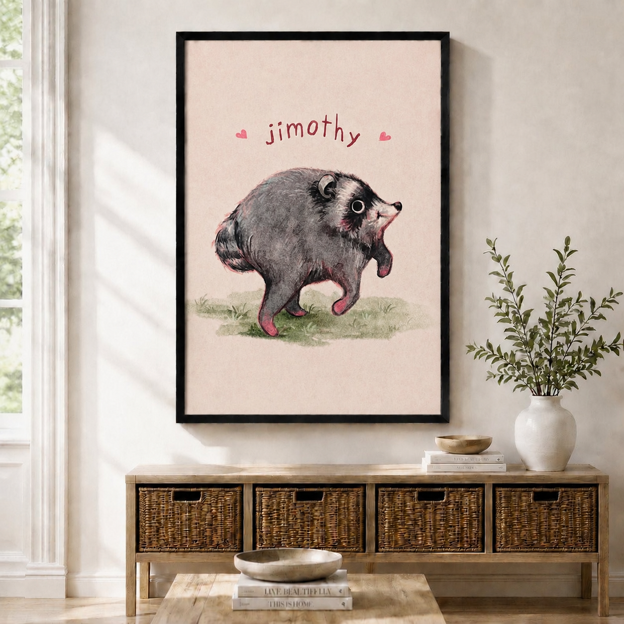 Cute framed wall art print of Jimothy the cartoon opossum with pink hearts on a blush pink background, displayed above a wooden console table with wicker baskets in a bright entryway