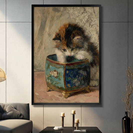 Black framed vintage calico kitten peering into a blue floral porcelain pot classical oil painting canvas wall art with warm beige background displayed in a modern gray living room with dark sofa and gold candlestick holders