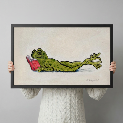 Hand-held preview of lazy frog reading book canvas art in black frame showing full whimsical illustration with spotted green frog and red book on textured cream background

