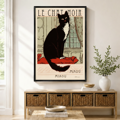 Framed Le Chat Noir Miaou vintage French black tuxedo cat poster wall art displayed above wicker storage console table in bright natural American entryway