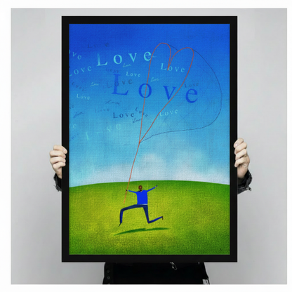 Hand-held framed canvas print of figure running with heart-shaped love kite against blue sky green meadow
